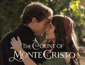 Actors Sam Claflin as Edmond Dantès and Ana Girardot as Mercedes stand in a sunlit garden, leaning their foreheads together with eyes closed in an intimate embrace. Edmond wears a dark, high-collared period coat, while Mercedes has a red headscarf tied over her dark hair.