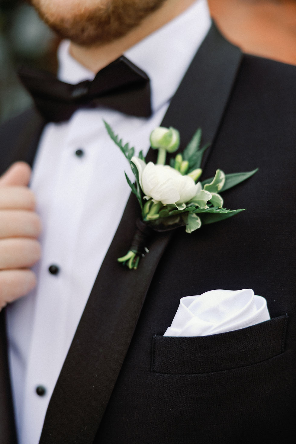 Close-up detail shot of a groom in a black tuxedo with a white rose and tulip boutonniere.
