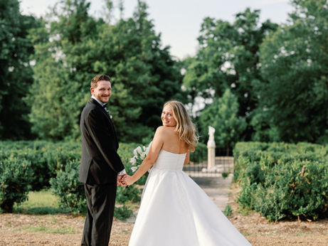 Bride in a strapless satin ballgown and groom in a black tux looking over their shoulders smiling at their Two Rivers Mansion wedding.