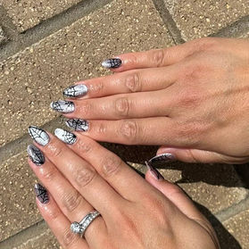 Acrylic nails featuring silver glitter polish with intricate black spider web design.