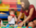 A toddler playing with a toy in a play area with a woman. 