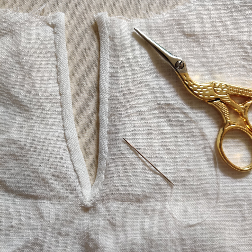 A pair of stork snips on white linen with a needle and thread