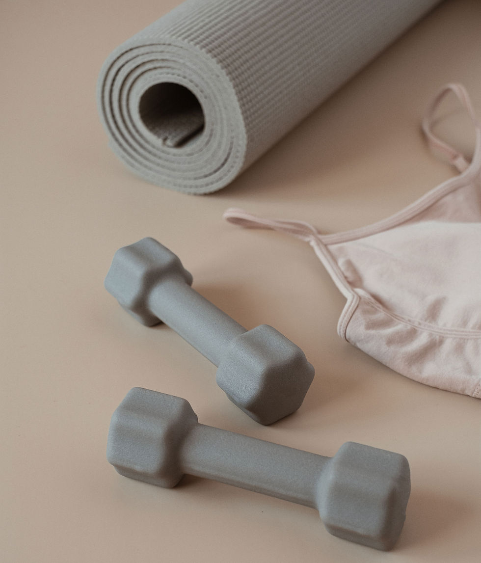 Gray dumbbells, a rolled yoga mat, and a pink sports bra on a beige surface, creating a calm fitness setup.