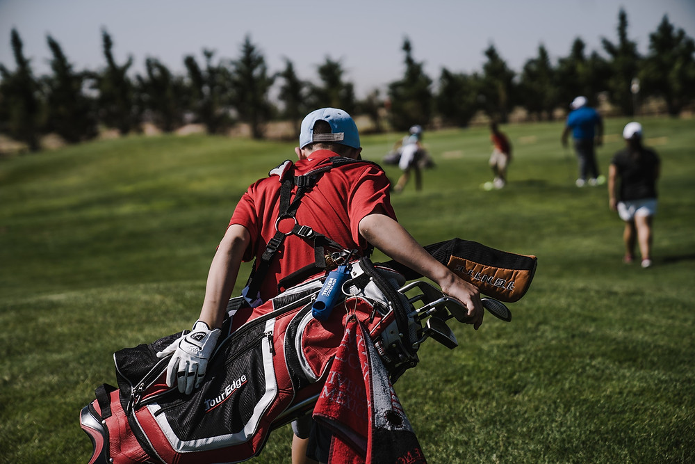 Photo of a caddy carrying a golf bag filled with clubs behind a group of golfers.