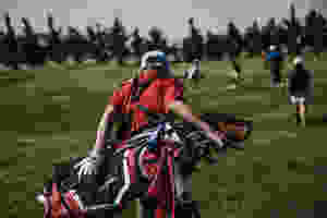 Photo of a caddy carrying a golf bag filled with clubs behind a group of golfers.