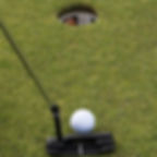 Photo of a golf ball on the green a few feet from the cup and a putter poised to tab the ball into the hole.