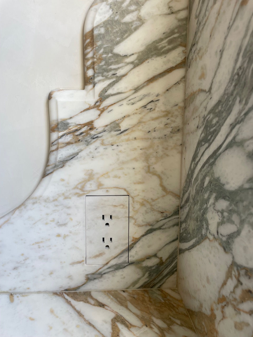 Marble wall with brown and gray veins, featuring a seamless electrical outlet matching the marble pattern. Elegant, sophisticated design.