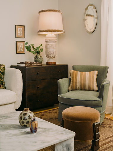 Eclectic living room corner designed by Stefani Stein, featuring a green linen armchair, burl wood dresser with vintage alabaster table lamp, marble coffee table, and layered textures.