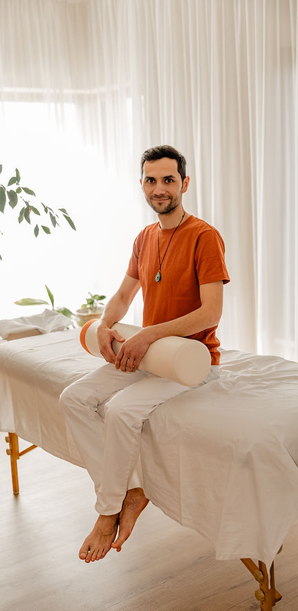 Mann sitzt auf Massagebank, lächelt freundlich, Hände auf den Beinen.