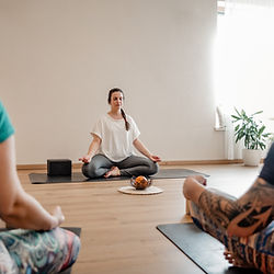 Yoga-Lehrerin leitet Meditation mit Schülern in hellem Raum. Yoga, Meditation praktizieren.