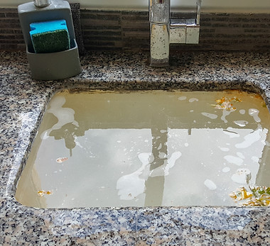 Overflowing kitchen sink, clogged drain with grease and food.