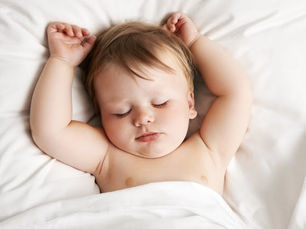 A toddler sleeping in a crib on a white blanket