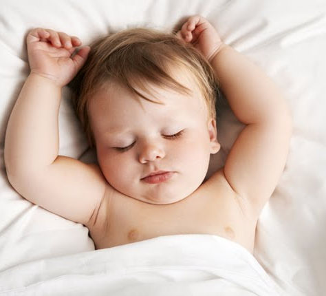 A toddler sleeping in a crib on a white blanket