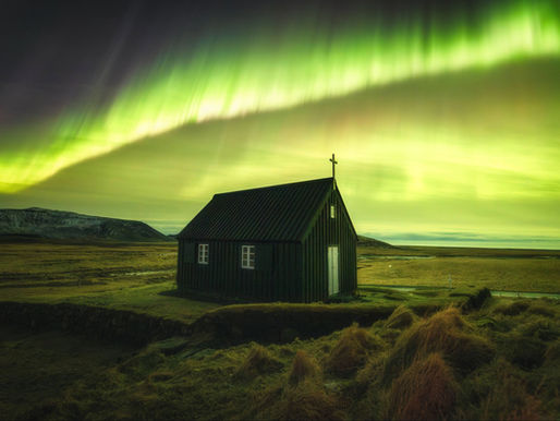 a powerful green aurora above a small wooden Icelandic church