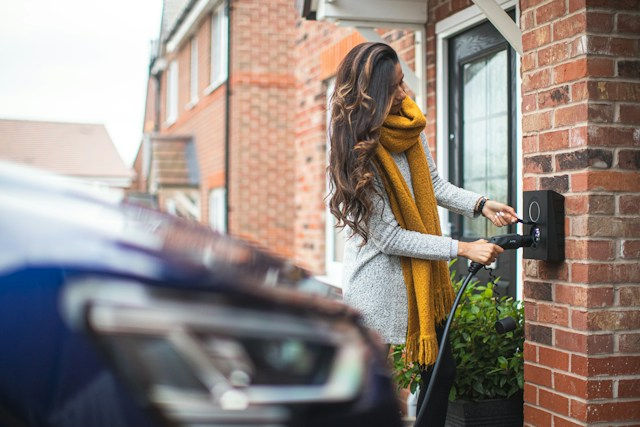 Woman wearing a woolly jumper plugging in her EV to charge