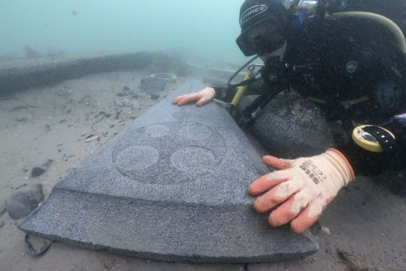 An intricately carved 13th century gravestone being examined by a diver