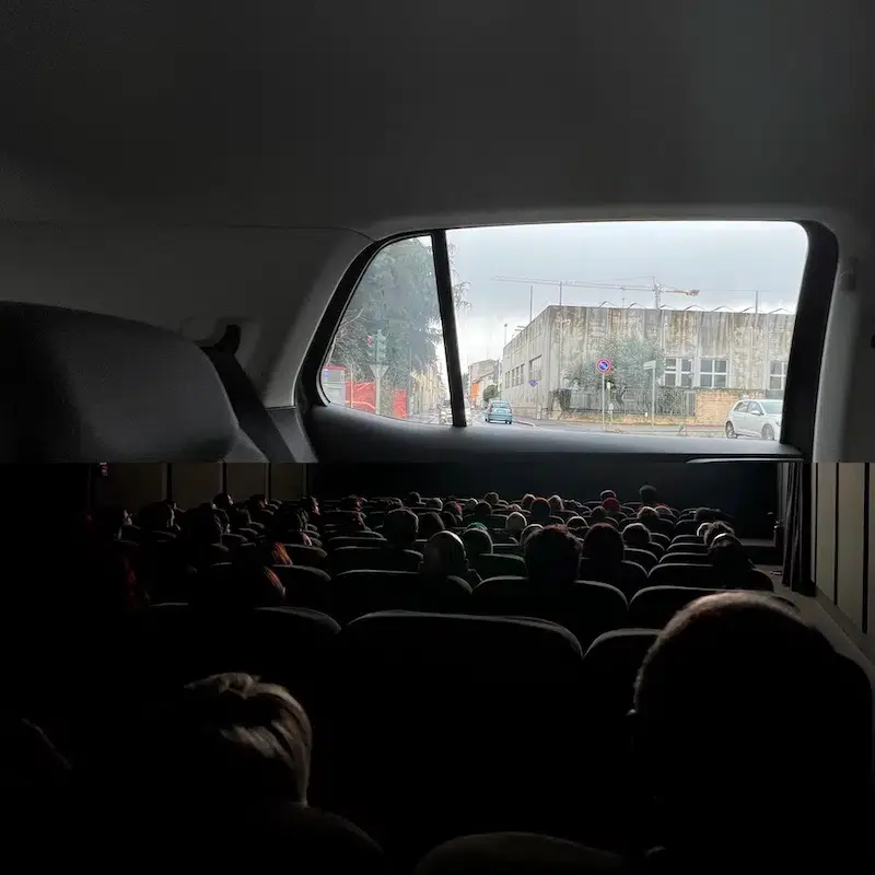Movie theatre full of people looking at a screen that is shaped like a car window