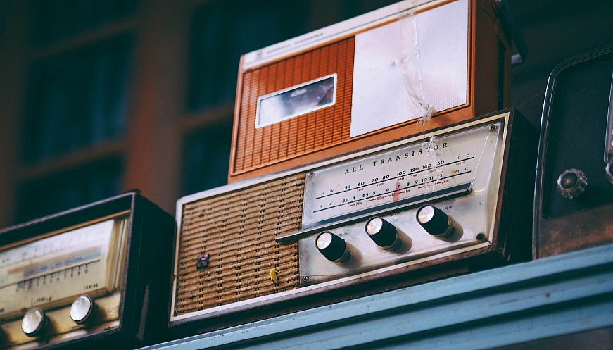 A couple of old radios sitting on a cupboard shelf.