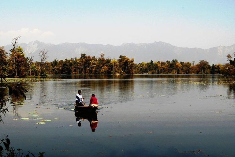 Man paddling a canoe across a lake with the foothills of the Himalayas in the background
