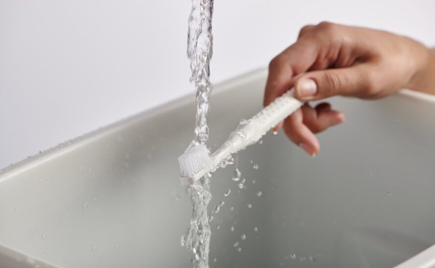 White toothbrush being rinsed under a basin tap