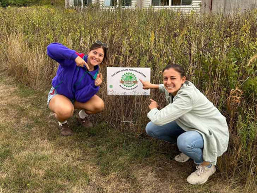 Mackenzie Feldman and Bridget Gustafson kneeling down next to a Green Grounds certification sign