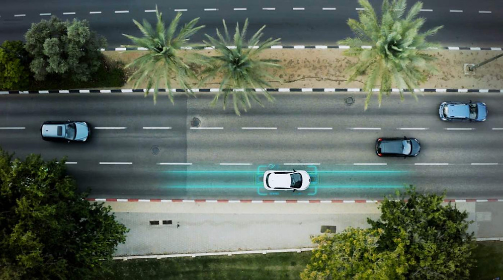 Aerial shot of a car travelling along a road that's been edited to show an blue electric glow