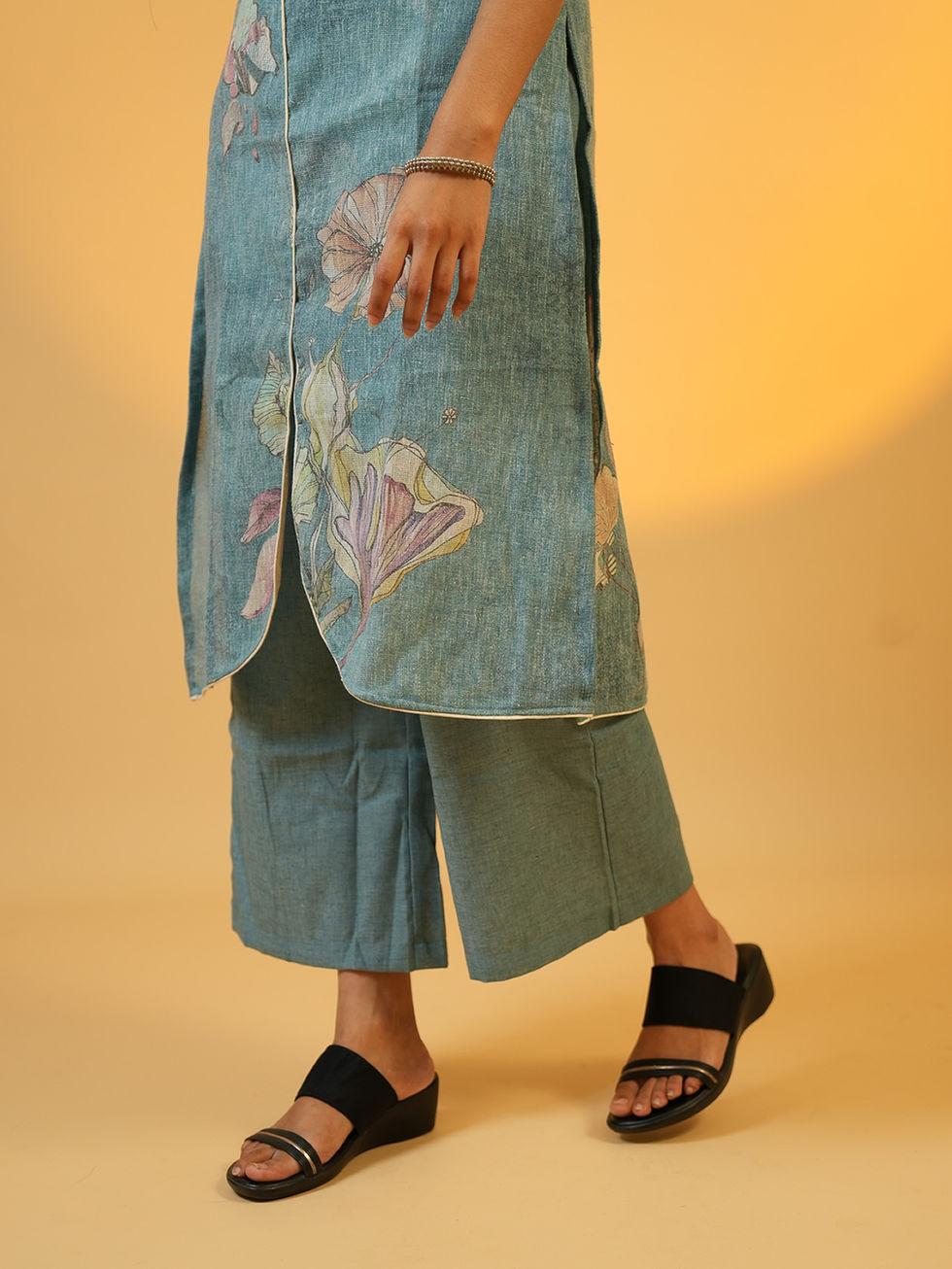 Close-up of person in blue patterned kurta set and black sandals.