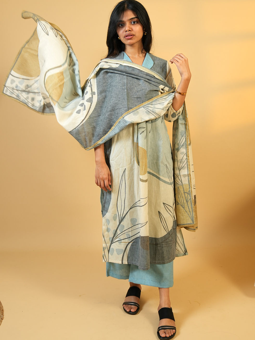 Woman models light blue and beige patterned kurta set with draped dupatta.