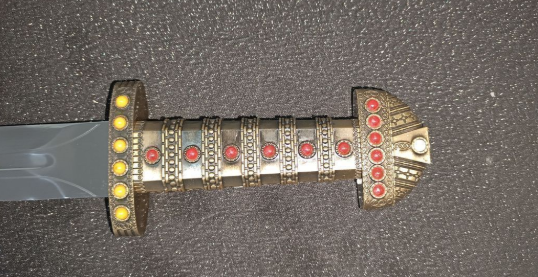 Miniature : Détail de la poignée de l'épée royale Vikings. Finition dorée avec incrustations de pierres rouges et textures ciselées.