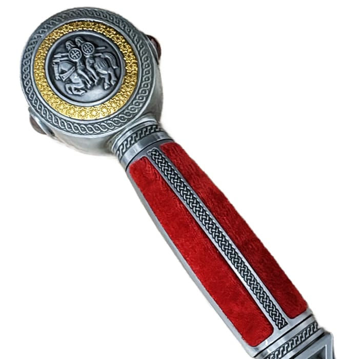 Miniature : Gros plan sur le pommeau gravé et la poignée rouge velours de l'épée médiévale. Détails héraldiques dorés et argentés.