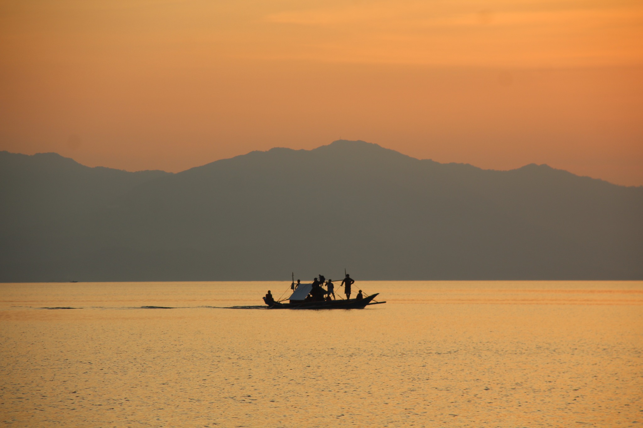 Small local boat crossing calm water at sunset