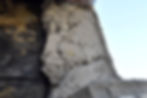 Close-up of rough gray plaster or concrete crumbling on a blackened surface against a pale blue sky