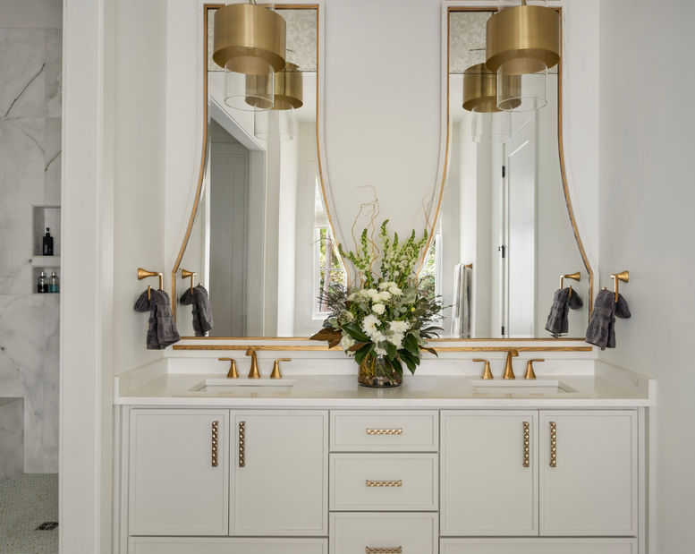 Luxurious bathroom vanity with two curved mirrors, gold accents, and a floral centerpiece. Interior Design project in the Serenbe community in Chattahoochee Hills, Georgia.