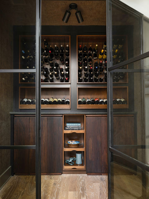 A glass-enclosed wine storage area with wooden racks full of wine bottles and shelving with decorative items.  Interior Design project in the Serenbe community in Chattahoochee Hills, Georgia.
