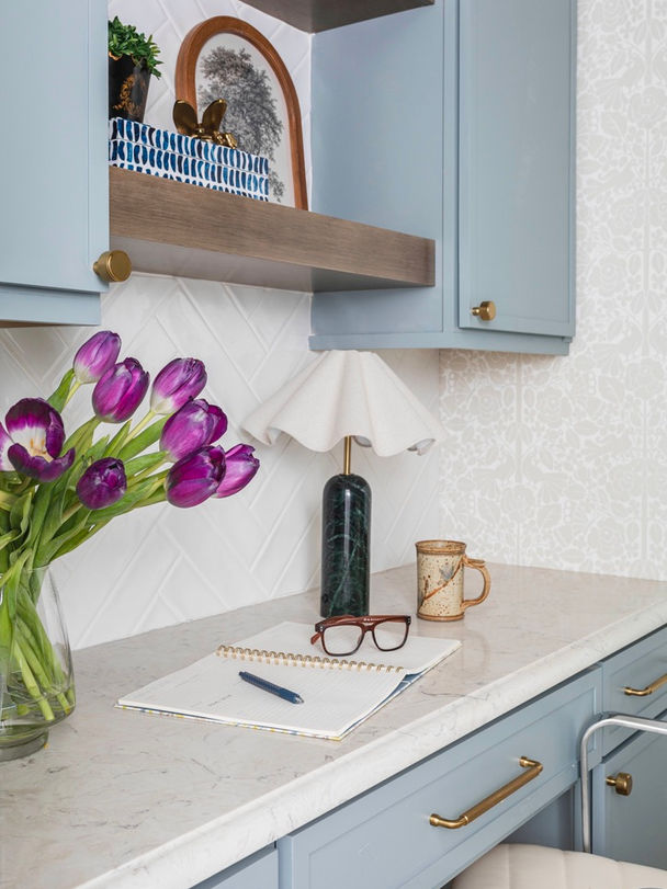 Custom home office nook in Senoia, GA with blue built-in cabinetry, brass accents, marble-look countertop, floating wood shelves, and fresh tulips styled on a compact workspace.
