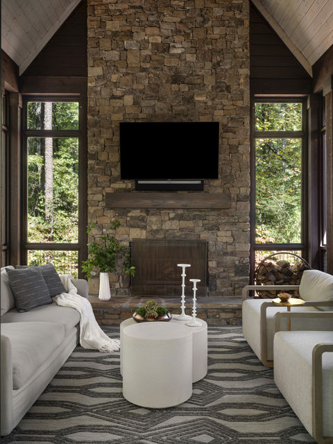 Living room with stone fireplace, sofas, and large windows offering an outdoor view. Interior Design project in the Serenbe community in Chattahoochee Hills, Georgia.