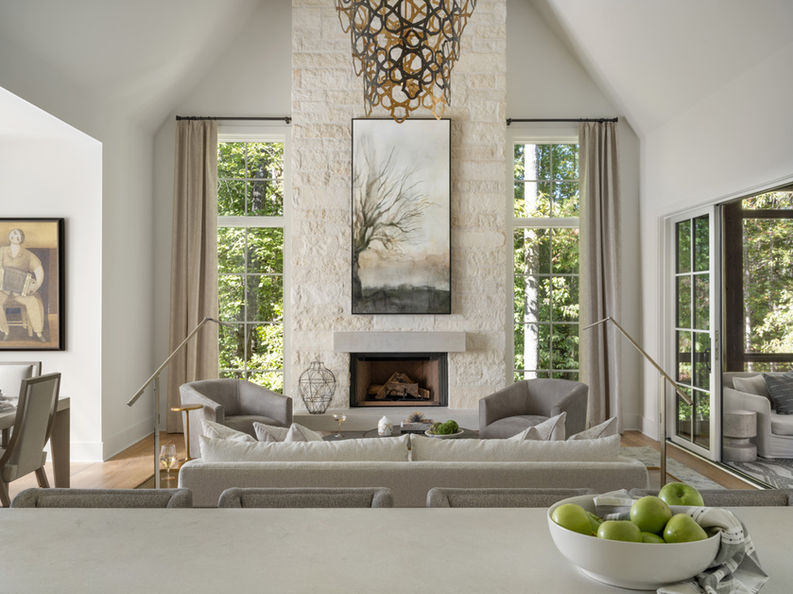 Living room with a stone fireplace, framed painting, and grey furniture, illuminated by natural light. Interior Design project in the Serenbe community in Chattahoochee Hills, Georgia.