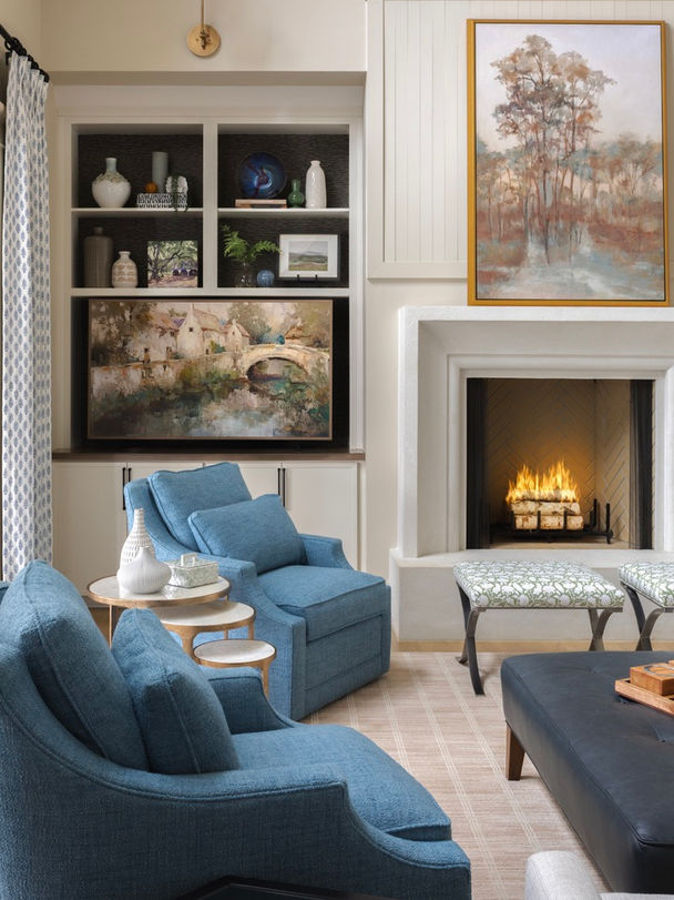 Cozy living room seating area in Senoia, GA featuring blue upholstered armchairs, built-in cabinetry, fireplace with landscape art, and layered neutral textures.
