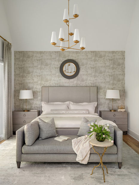 Modern bedroom with a gray bed, sofa, and light wood bedside tables, featuring a chandelier and mirror. Interior Design project in the Serenbe community in Chattahoochee Hills, Georgia.