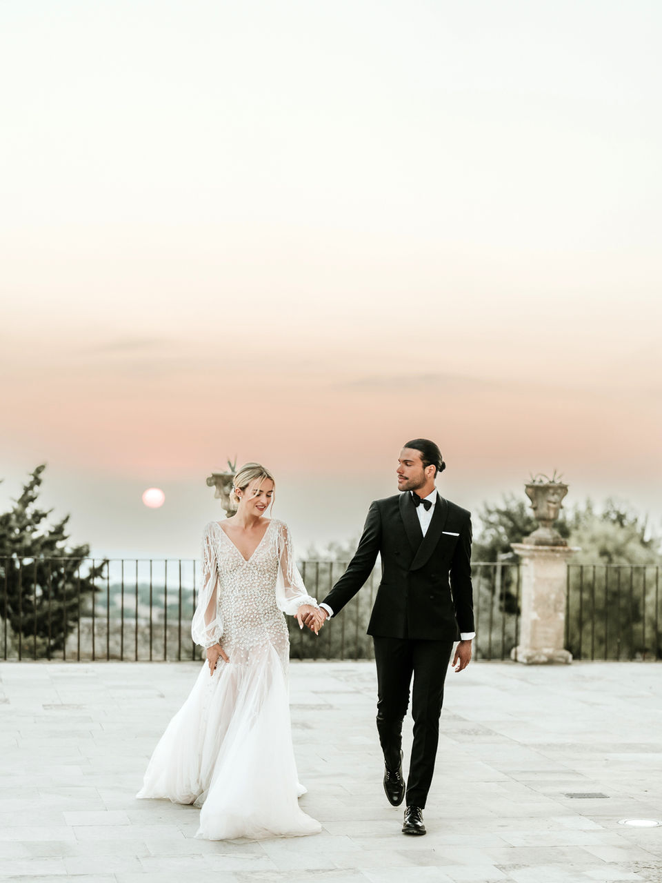 Sur la terrasse d'un palis sicilien, un couple marchant main dans la main devant le coucher de soleil. Photographe de mariage Sicile, France, Provence