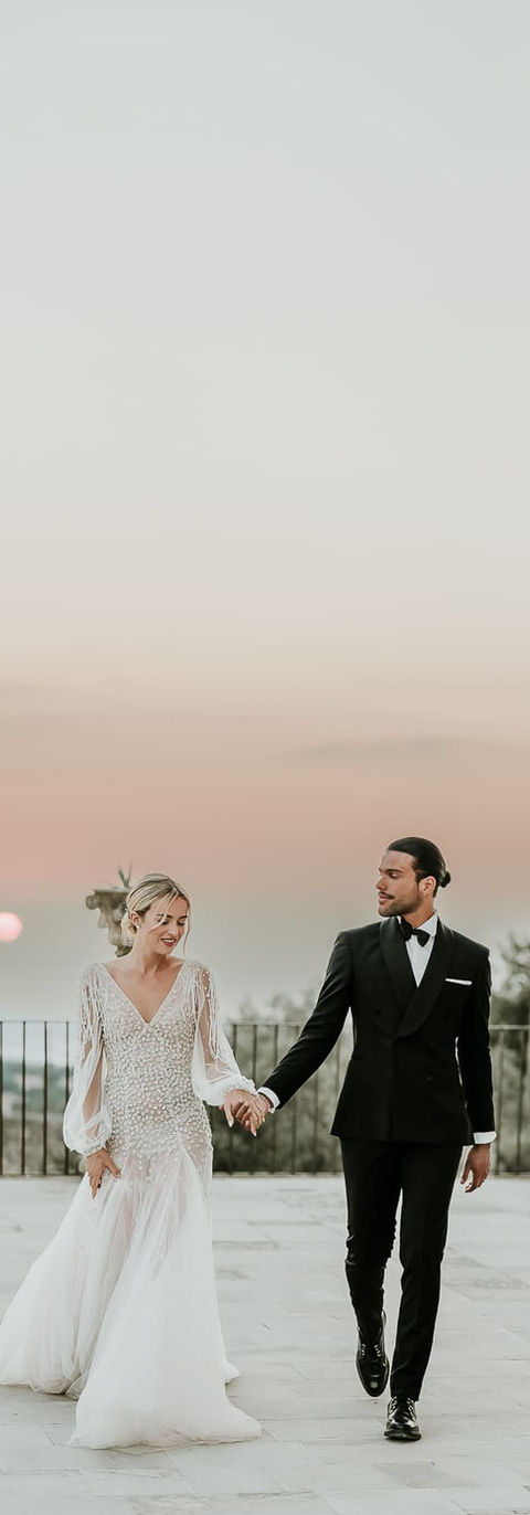 Au coucher du soleil, sur la terrasse d'un palais sicilien, un coiuple marche main dans la main en souriant - destination wedding photographer Sicile, Italie, French Riviera