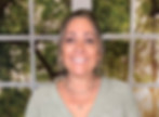 Smiling woman standing at a rustic craft table with a window backdrop of green trees.