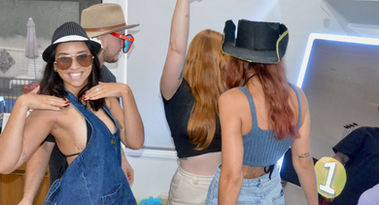 Four people having fun in a photo booth at a party. One person in the foreground poses with a big smile and sunglasses, while others are dancing and wearing hats, creating a lively and carefree environment.