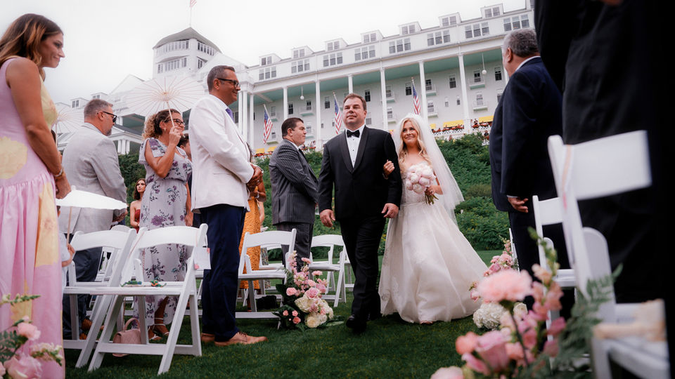 A father walking the bride down the aisle in the Rose Garden with the Grand Hotel in the background.