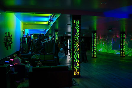 Modern indoor event venue with lounge seating, colorful LED lighting, and illuminated columns during a private event.