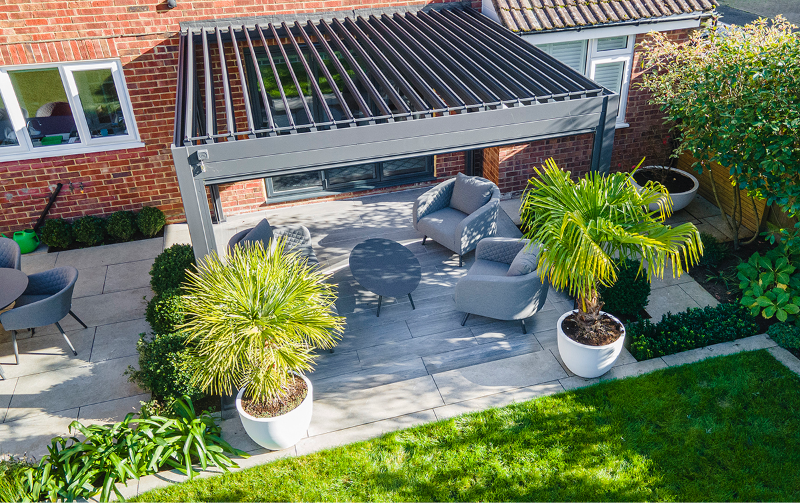 A modern metal pergola seamlessly integrates indoor and outdoor living spaces, offering a stylish and relaxing area with comfortable seating and lush greenery.