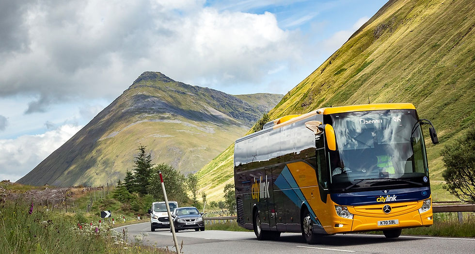 A bus travelling through a scenic valley in Scotland.