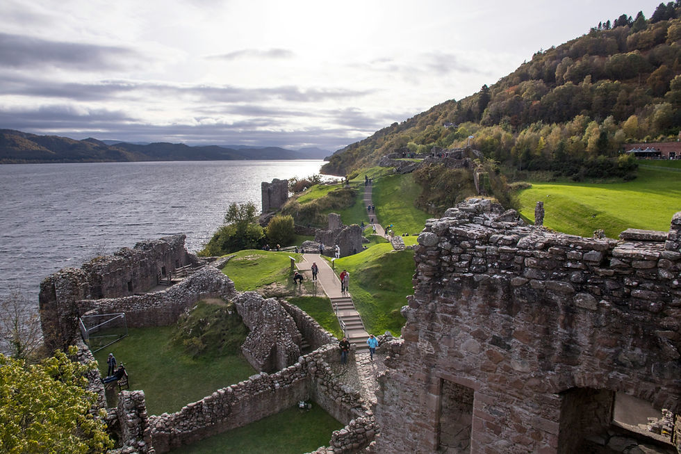 The ruins of a castle against a backdrop of trees and the shoreline of Loch Ness