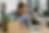 Man in blue shirt looking worried, sits at a desk with a laptop and a cardboard box. Woman working at a computer in the background. Office setting.