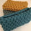 Thumbnail: a pile of small knotted cotton cord clutch bags in various colours, sage green, mustard yellow and teal blue
